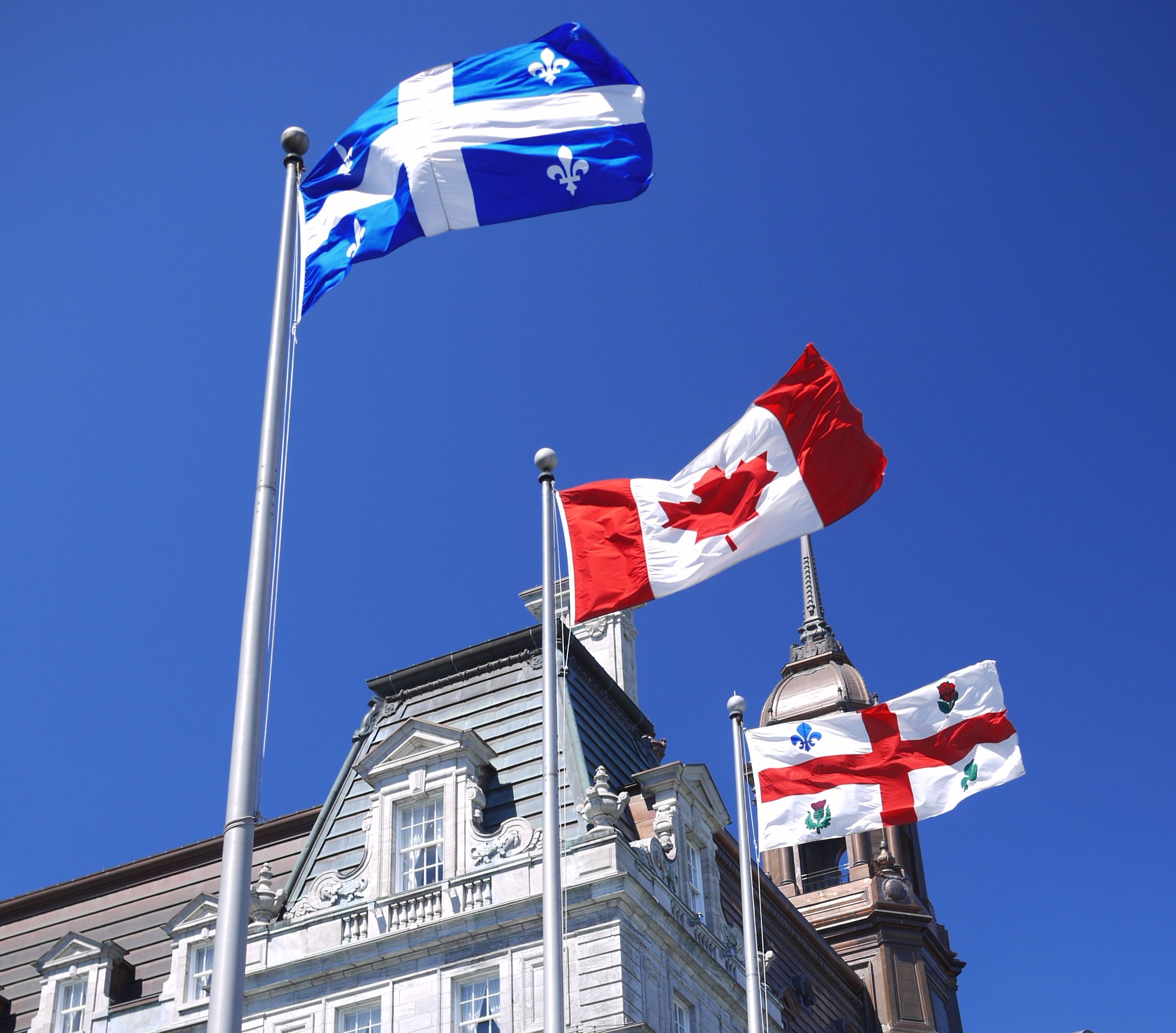Image from Wikimedia Commons Flags of Québec, Canada and Montréal against blue sky